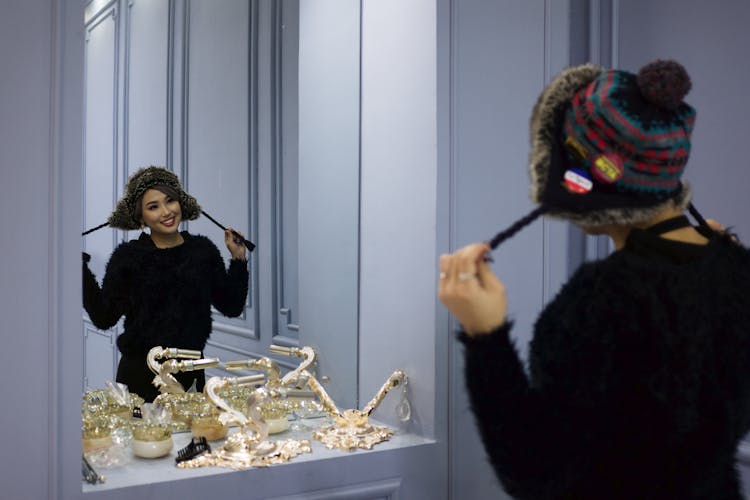 Woman Trying On A Woolen Hat In Front Of A Mirror