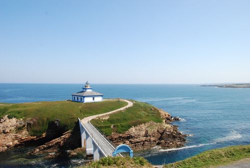 Free A beautiful coastal view featuring a lighthouse on a rocky cliffside with a clear blue sky. Stock Photo