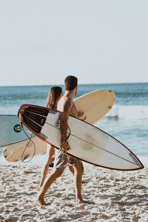 Free Two surfers carry their boards along a sandy beach in Rio de Janeiro, Brazil under the bright sun. Stock Photo