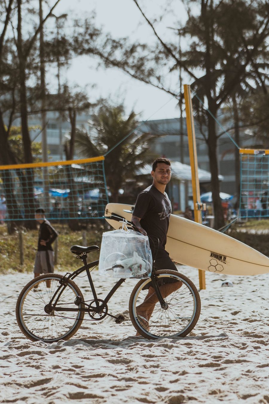 Surfer carrying a board and a bicycle on the beach
