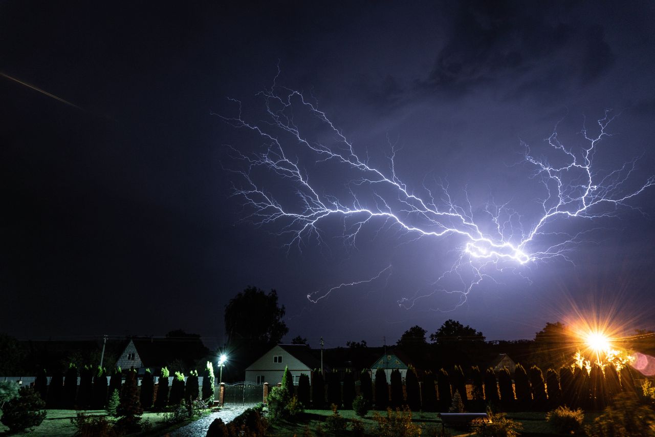 a powerful lightning bolt illuminates the night sky above a suburban n