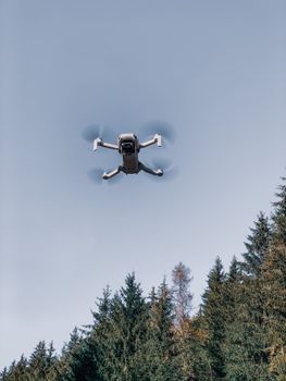From below of flying drone with blades spinning over green  forest with pines and spruce under clear blue sky