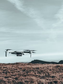 A modern drone flying over a serene grassy field against a dramatic sky.