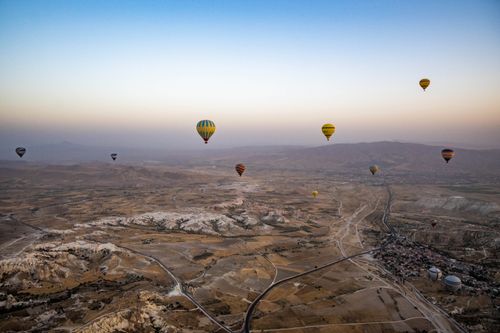 Free Scenic aerial view of hot air balloons floating over Cappadocia's unique terrain at sunrise. Stock Photo
