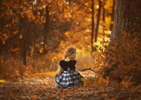 A young girl sitting amidst vibrant autumn leaves, embracing nature.