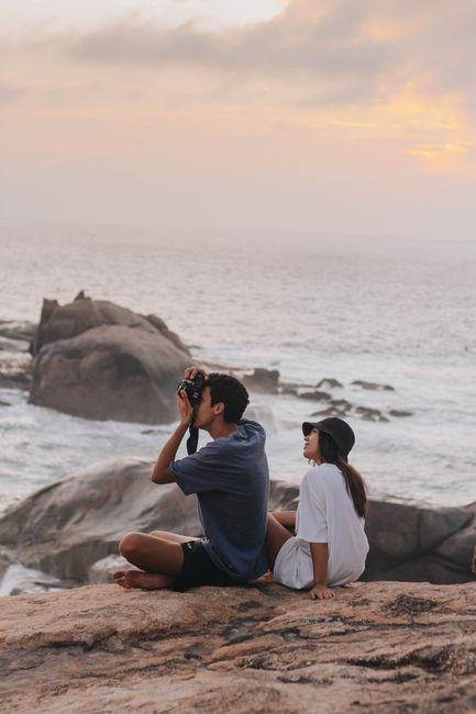 A couple sitting on rocky shore in Brazil, enjoying a sunset by the ocean.