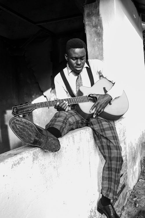 Free A young guitarist playing outdoors against a concrete wall in Takoradi, Ghana. Stock Photo