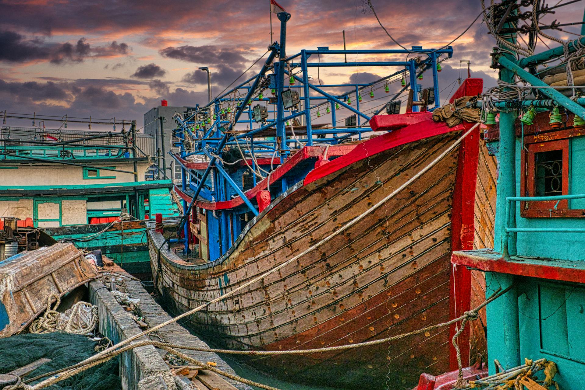 Traditional fishing boats docked at a vibrant port in Jakarta, Indonesia during sunset.