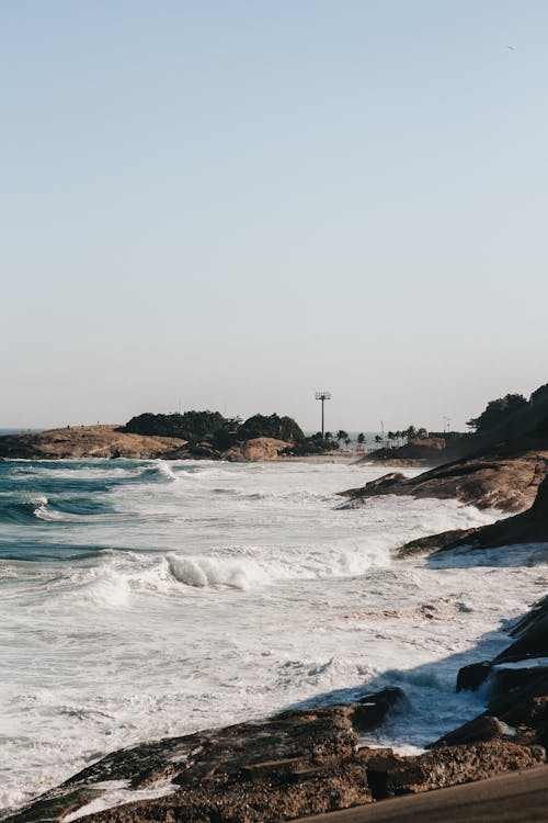 Free Explore the stunning rocky shoreline and crashing waves of Rio de Janeiro's scenic coast. Stock Photo