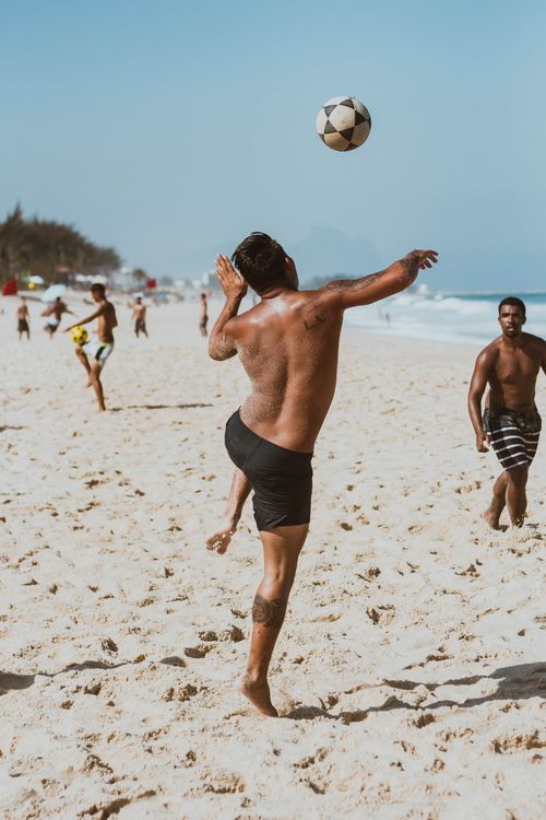 Free Men playing football on a sandy beach in Rio de Janeiro, Brazil under summer sun. Stock Photo