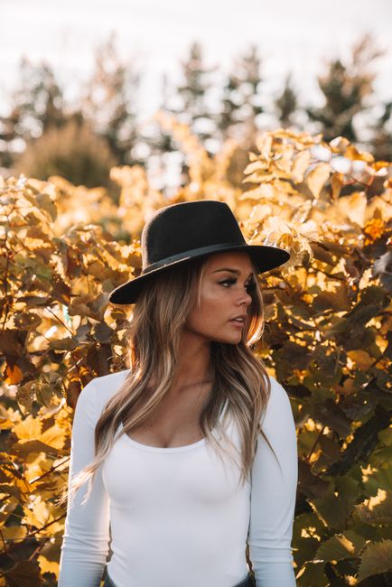 Trendy female with long hair wearing black hat and looking away against colorful yellow foliage