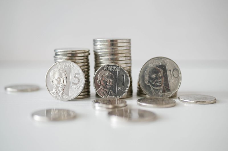 Stacked and scattered Philippine Peso coins in a close-up view on a white surface.