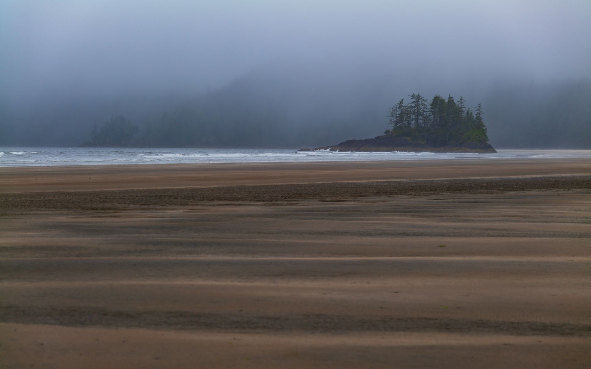A serene and foggy view of San Josef Bay with sandy beach and island, captured in British Columbia, Canada.