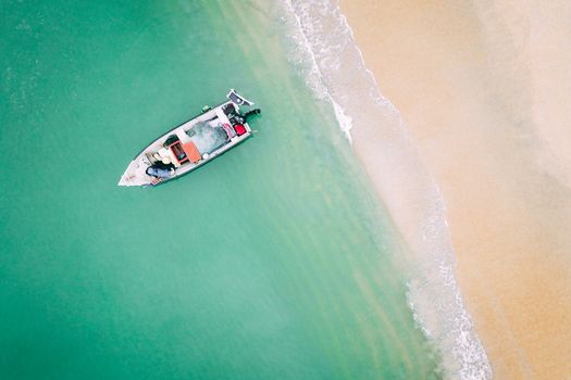 Top view of vessel sailing in turquoise water of foamy tranquil ocean with sandy beach