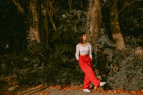 Free Full body of young woman in stylish clothes standing with raised leg in park with green trees and looking away in daytime Stock Photo