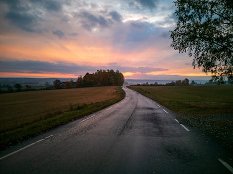 Tranquil rural road with fields under a vibrant sunrise sky, perfect for peaceful landscape themes.
