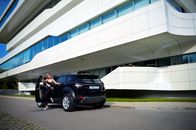 Full body attractive fit female driver in trendy wear standing gracefully near new black modern car outside contemporary office building