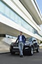 Confident man leaning on modern black car outside office building