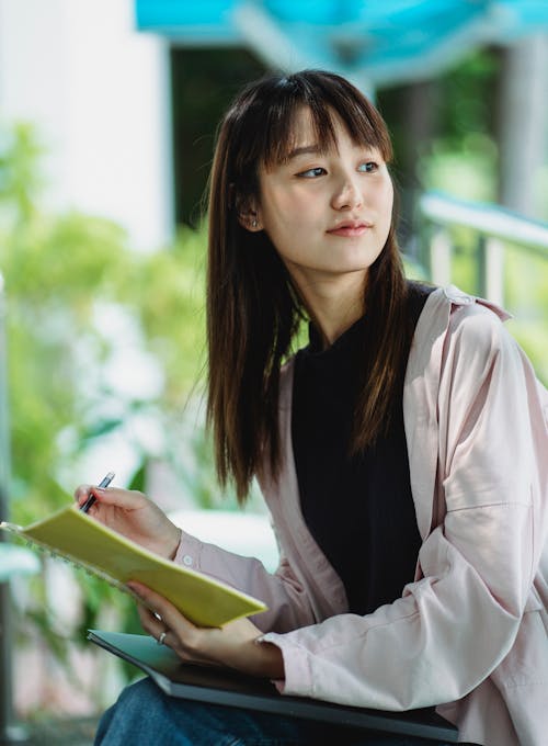 Dreamy Asian student with copybook on street