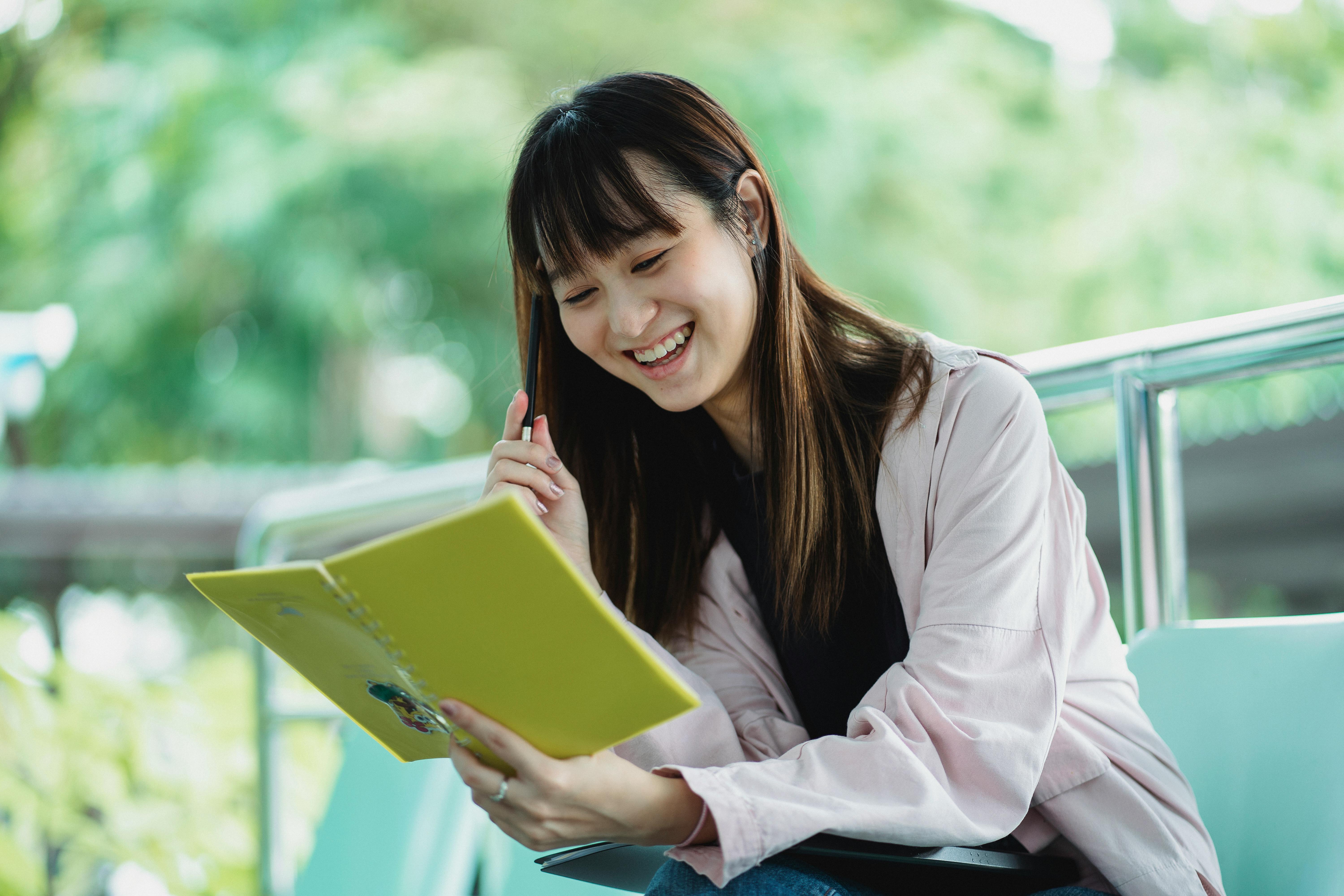 positive asian student with exercise book studying on street