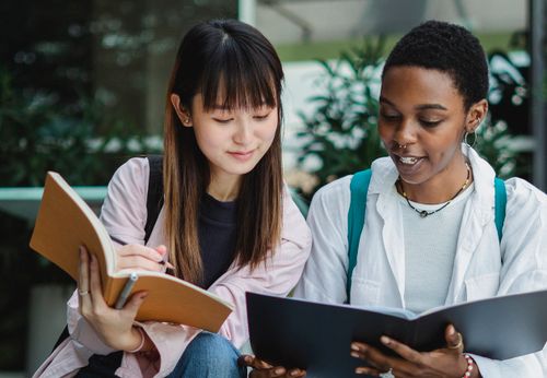 Free Young smiling black female student with exercise book talking to Asian partner on street in daylight Stock Photo