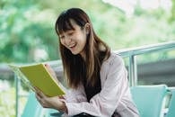 Cheerful Asian woman with workbook studying on chair