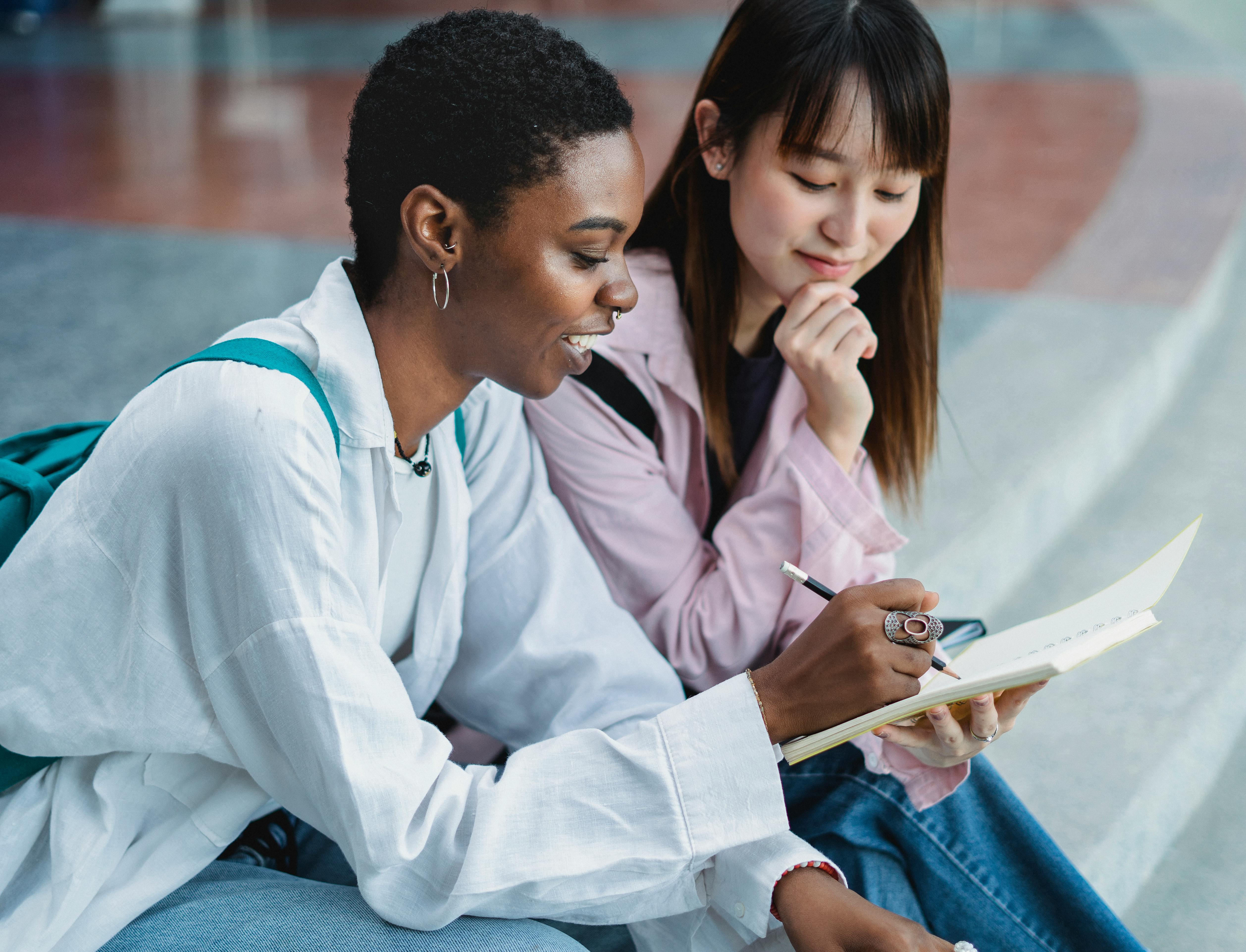 Smiling black woman sharing workbook with crop Asian girlfriend outdoors ·  Free Stock Photo