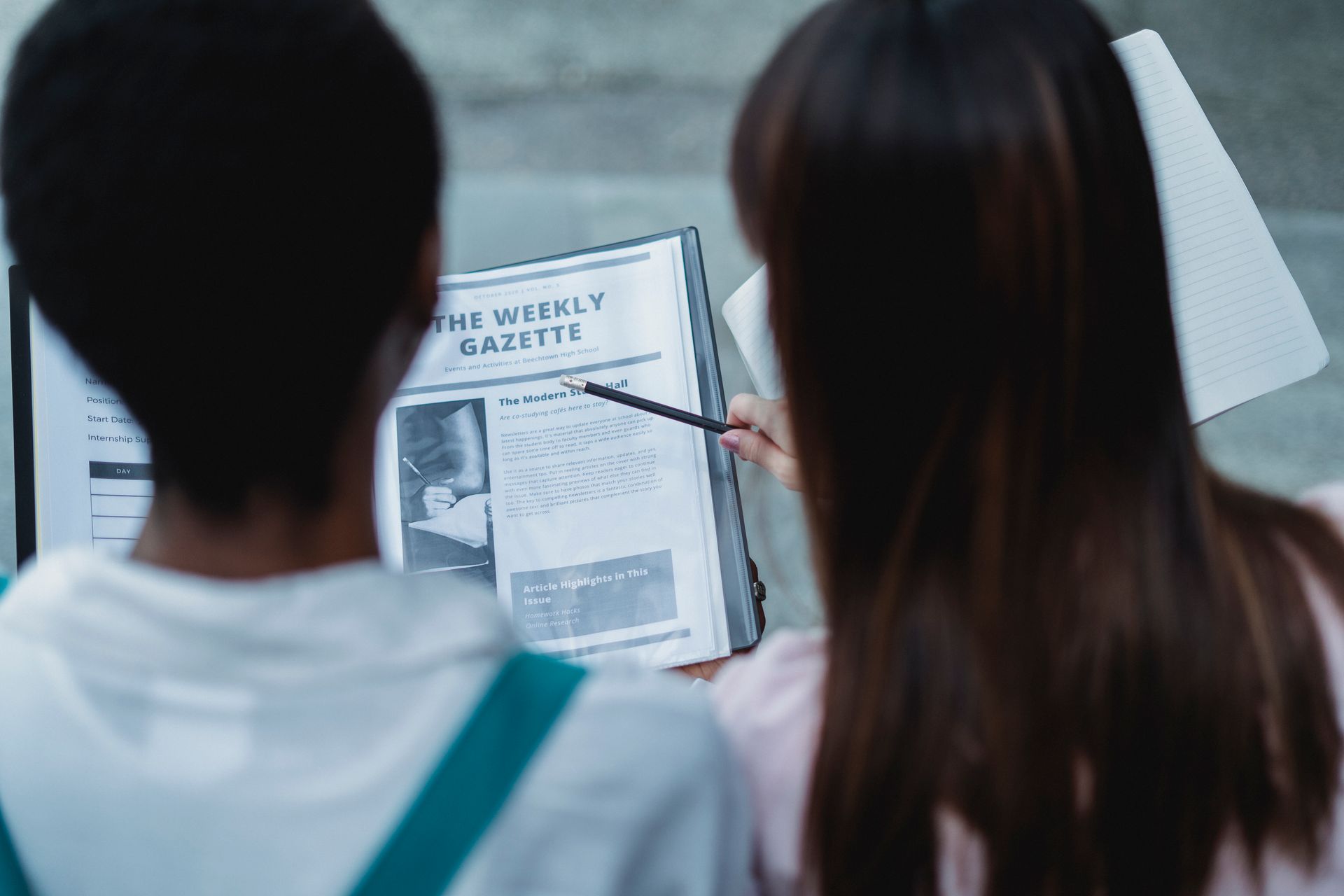 Two students discussing an article in The Weekly Gazette, focusing on learning and education.