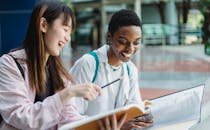 Crop laughing multiethnic girlfriends watching book in town