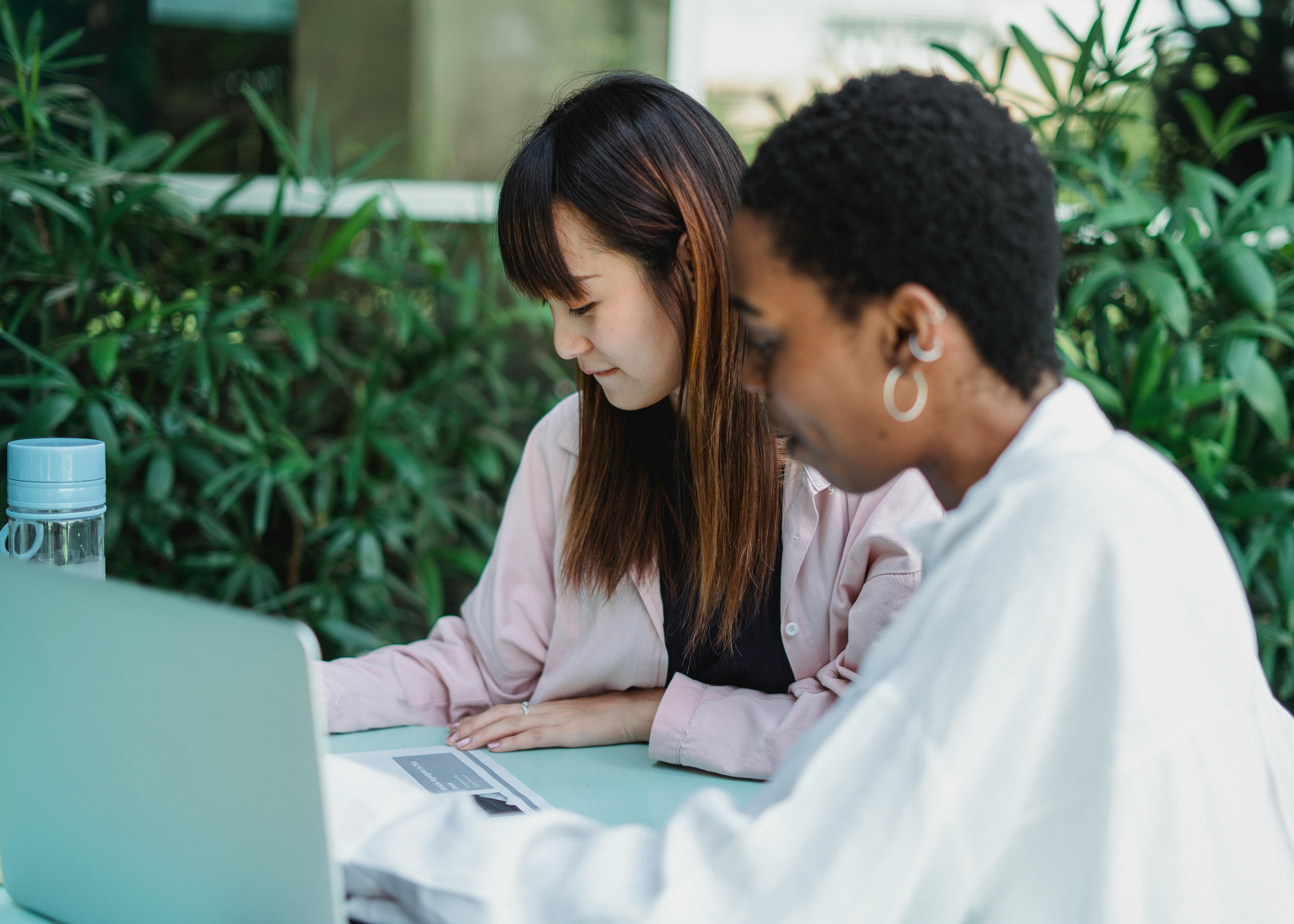 smiling multiracial students doing homework at table with laptop outdoors