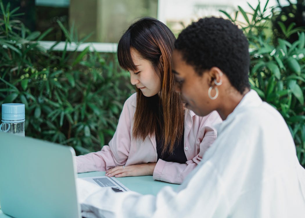 Smiling multiracial students doing homework at table with laptop outdoors