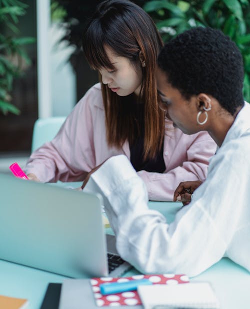 Multiethnic female students doing homework at table with laptop