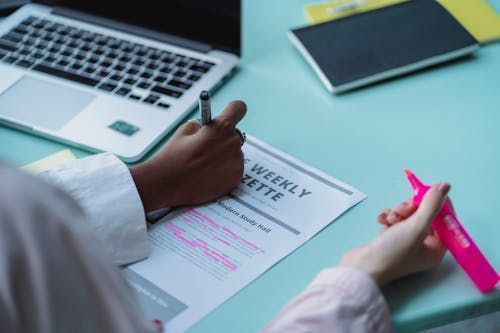 Free From above of crop anonymous ethnic woman taking note on paper sheet with text near anonymous friend at table with laptop Stock Photo