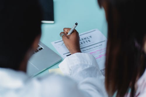 Crop black woman writing on paper near unrecognizable ethnic girlfriend