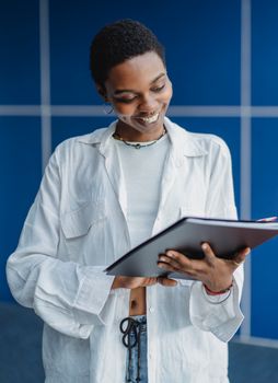 A young woman smiling while studying on a tablet indoors against a blue backdrop.