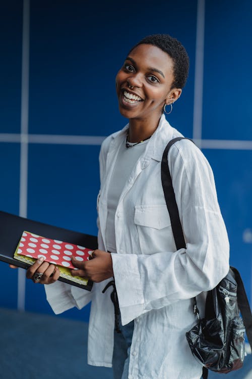 Positive black woman with workbooks near blue wall