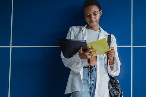 Free Crop young African American woman in casual outfit standing with open workbook near blue wall Stock Photo