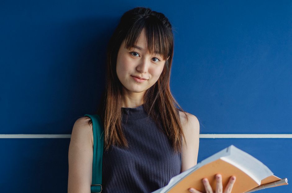 青い壁の近くに練習帳を持つ魅力的なアジアの学生