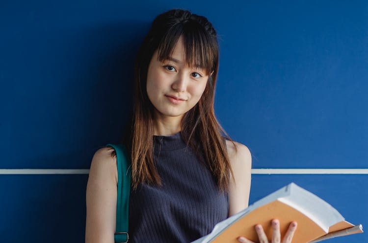 Charming Asian Student With Exercise Books Near Blue Wall