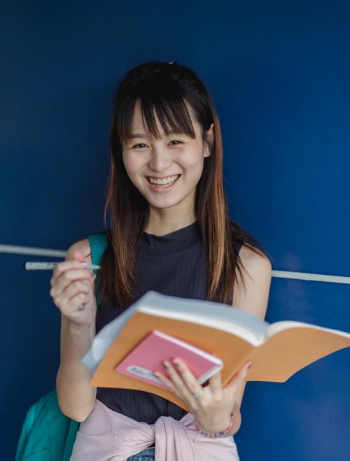 Free Young Asian woman smiling while studying with books indoors, embodying joy in education. Stock Photo