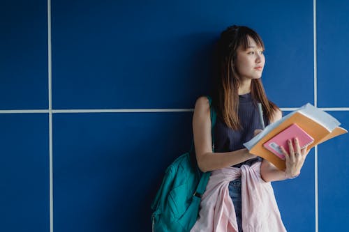Estudante Asiático Contemplativo Com Cadernos Perto De Parede De Azulejos