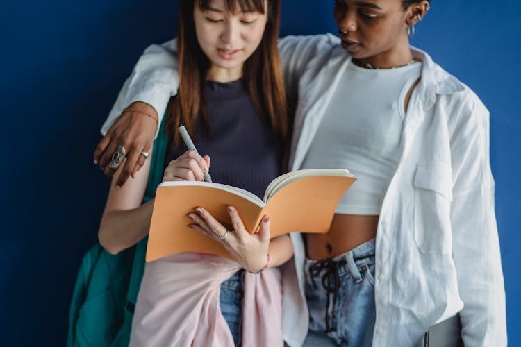 Crop Attentive Diverse Students Watching Workbook While Studying And Talking