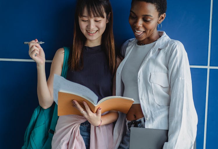 Crop Content Multiethnic Students Sharing Workbook While Studying Near Wall