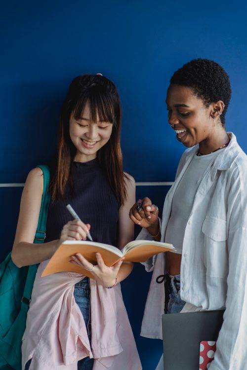 Free Young glad best diverse friends writing in exercise book while speaking near blue wall Stock Photo