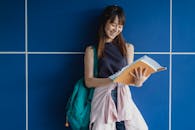 Happy Asian woman with workbooks studying near blue wall