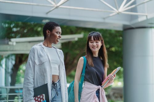 Free Young content multiracial students in casual clothes with workbooks talking under roof in daytime Stock Photo