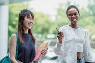 Cheerful multiracial girlfriends with workbooks speaking in daylight