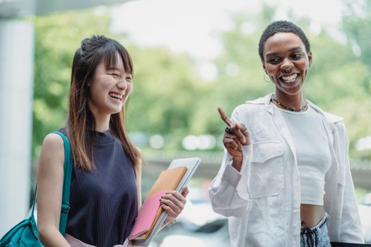 Cheerful multiracial girlfriends with workbooks speaking in daylight