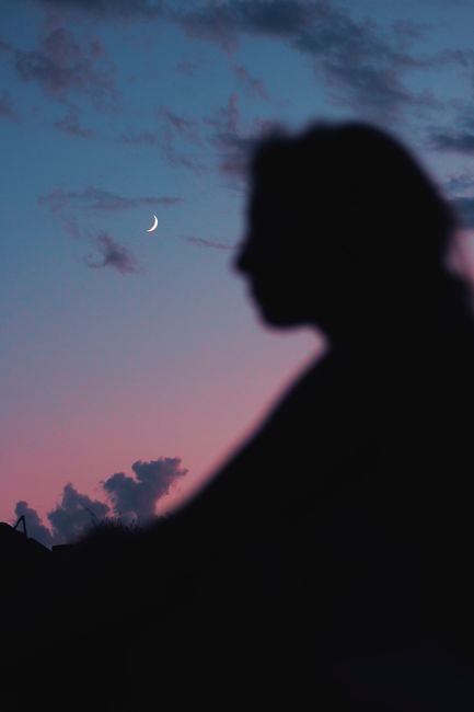Silhouette of a person against a crescent moon and twilight sky in Selinunte, Sicily.