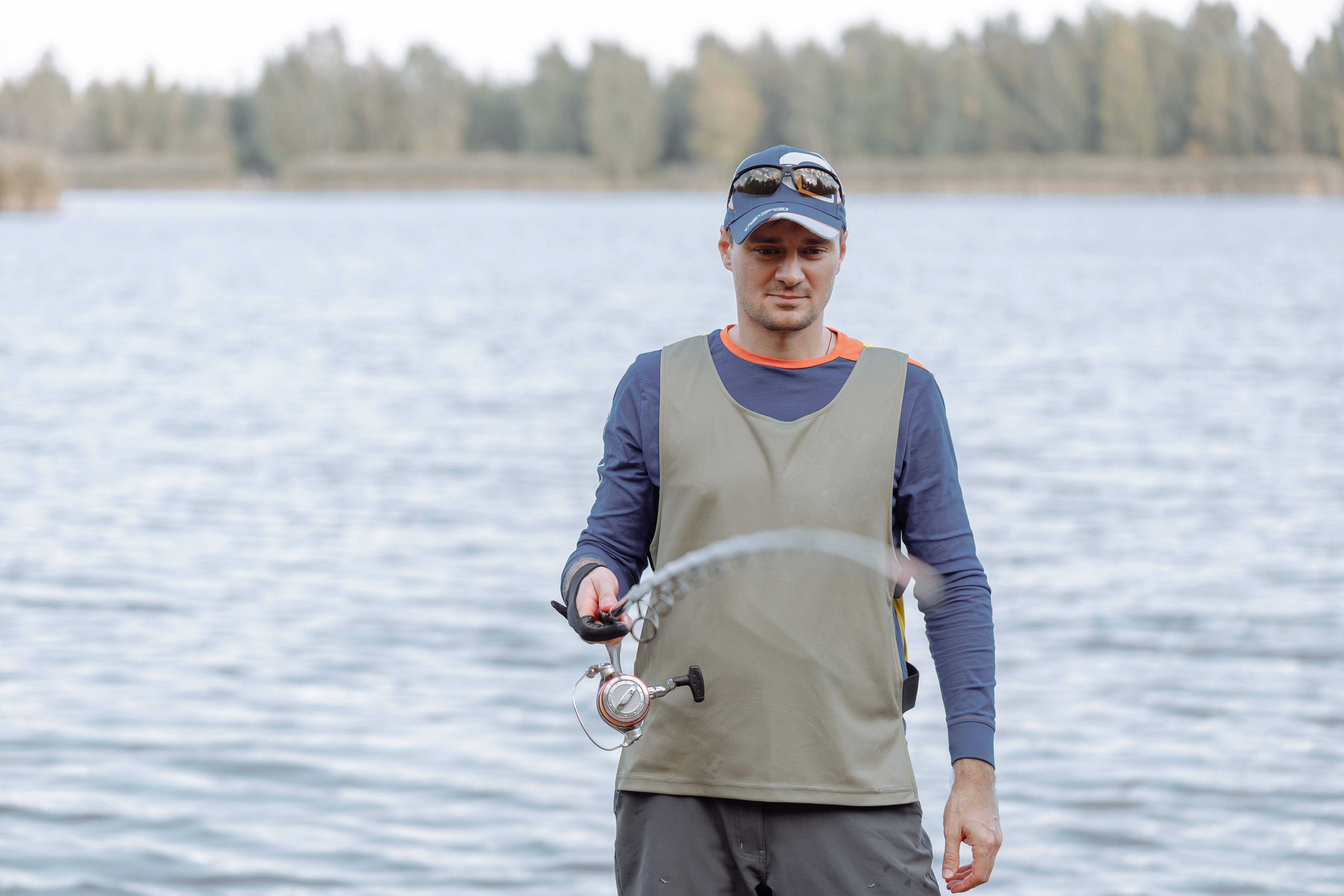 Man holds a fishing rod by a scenic lake, enjoying a peaceful outdoor hobby.
